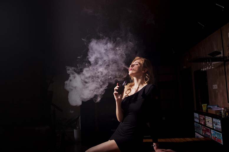 Vapes entsorgen: Junge Frau dampft eine E-Zigarette in einer Bar, eine Dampfwolke steigt auf