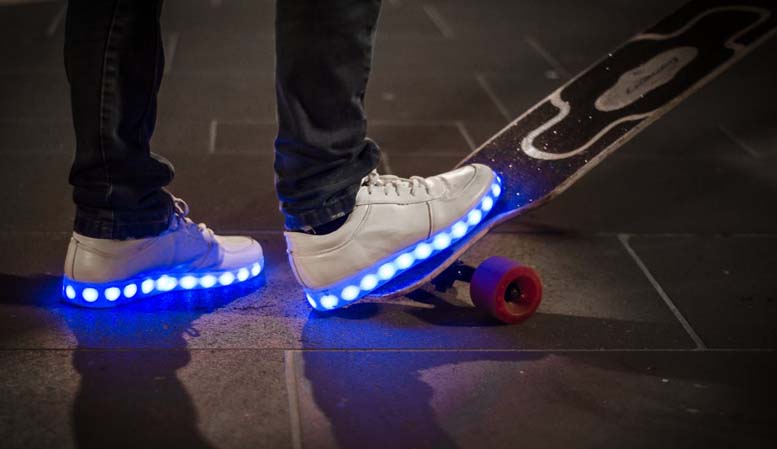 Beine in blinkenden Turnschuhen mit leuchtenden Außensohlen, ein Fuß steht auf einem Skateboard