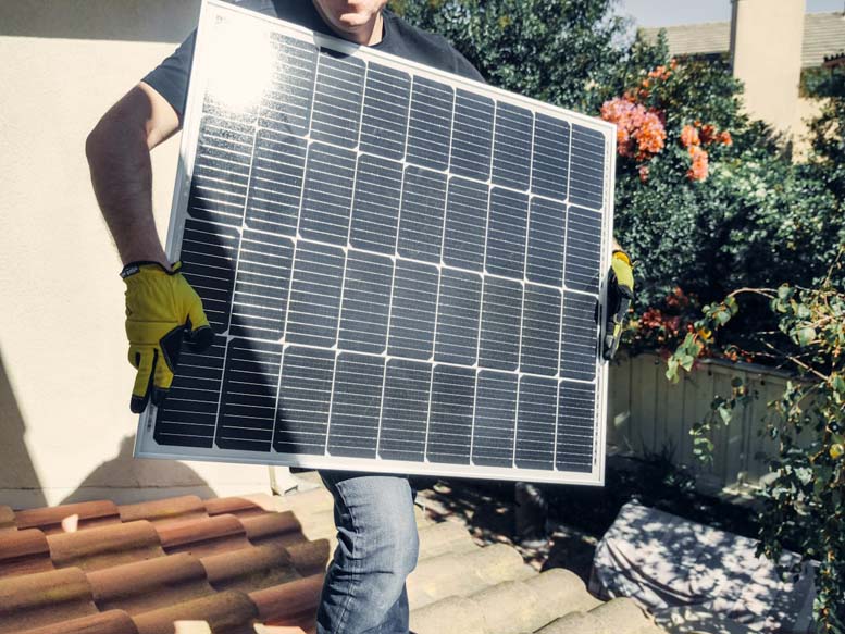 Mann steht auf einem Hausdach und hält ein Solarmodul zur Entsorgung in den Händen